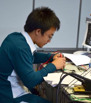 Un apprenti en CAP Electricien est penché sur sa table de travail, entre des instruments de mesure et des feuilles de note.